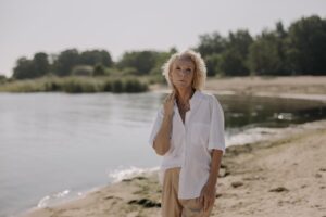 a mature woman in a white shirt standing by a lakeside
